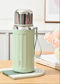 A 530ml spruce green insulated water bottle with a stainless steel lid and carrying loop, displayed on a matching silicone coaster on a wooden table. The image includes feature callout graphics on the left and a soft home background with books and flowers on the right.