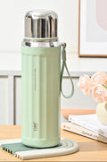 A mint green insulated water bottle with a stainless steel lid and wrist strap, shown on a tabletop with decorative flowers and books in the background. The image includes feature callout graphics on the left and text reading 'Spruce green' and '630ml'.