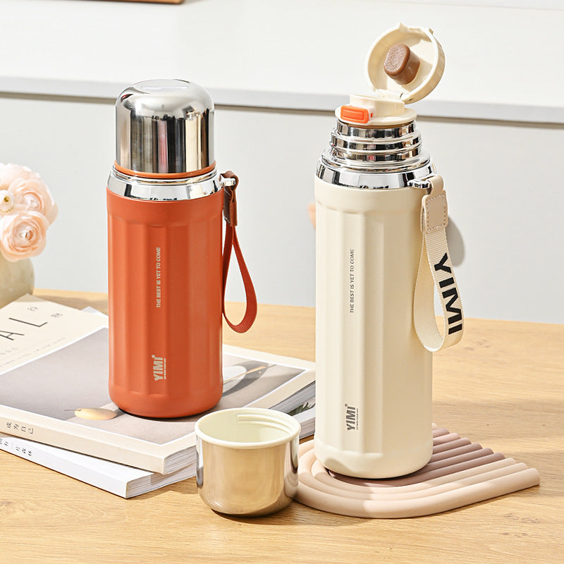 A cream-colored vacuum insulated water bottle with a shiny silver stainless steel lid and a matching carrying strap, shown on a plain white background.